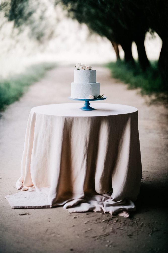 elegancki minimalistyczny dwupietrowy tort z kwiatowa dekoracja na okraglym stole z rozowym obrusem na weselu w plenerze we wloszech